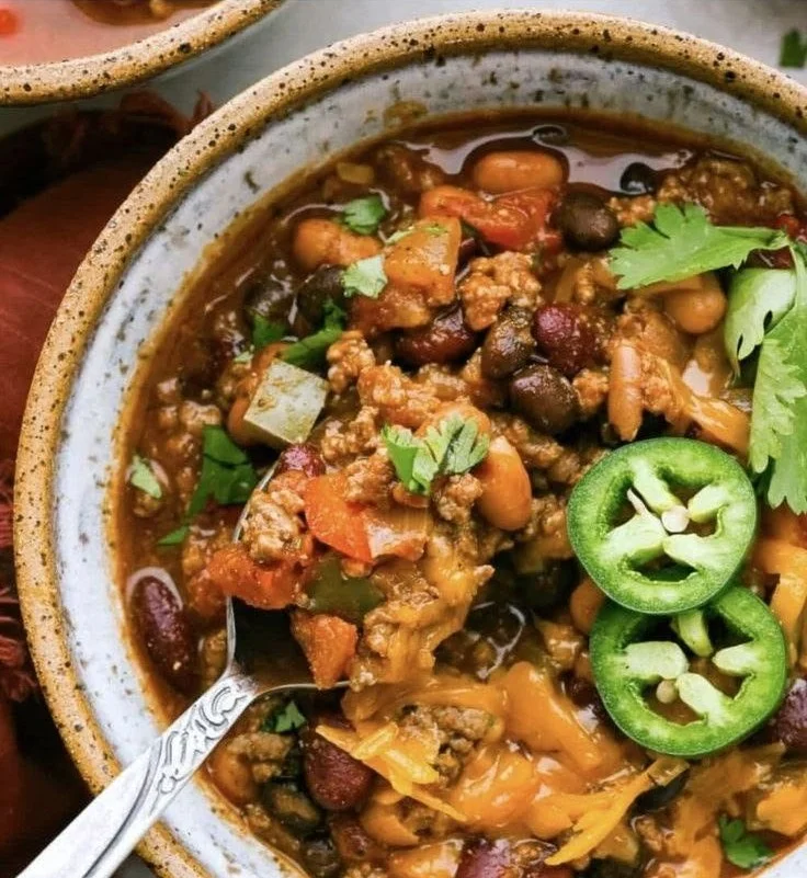 Bowl of spicy chili topped with cheese and herbs
