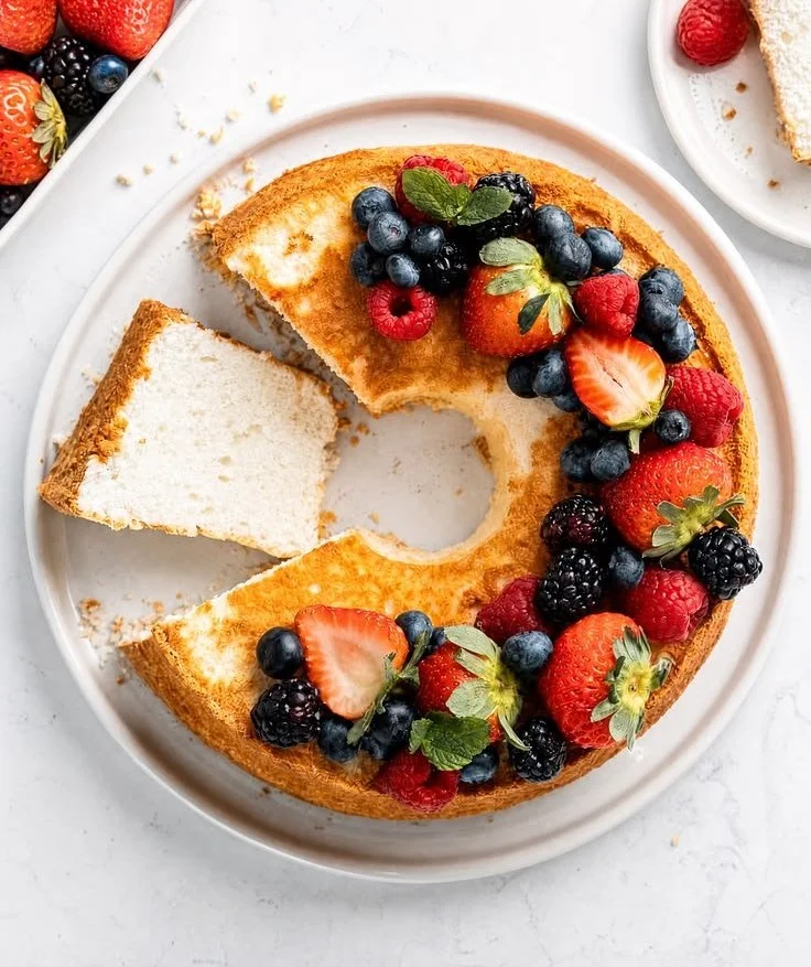 Homemade angel food cake topped with fresh berries on a white plate